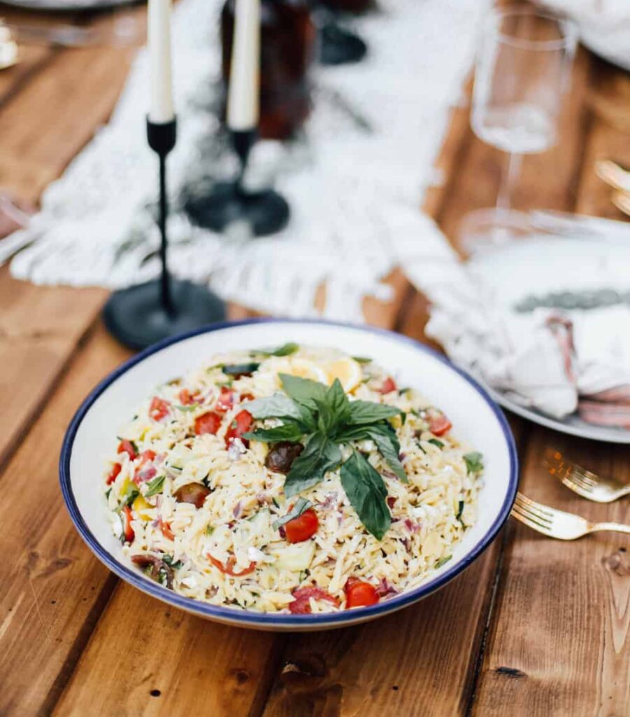 Orzo Pasta sits on wooden table and surrounded with candlesticks